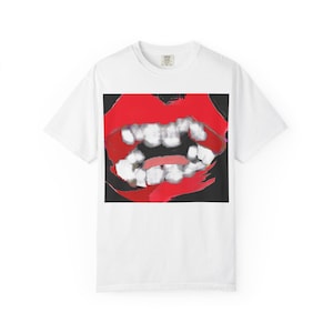 Może przedstawiać: Biały t-shirt z krótkim rękawem z dużym, wyśrodkowanym nadrukiem graficznym przedstawiającym parę jaskrawoczerwonych ust z białymi zębami na czarnym tle. Wzór ma malarski, teksturowany wygląd z widocznymi efektami pociągnięć pędzla.