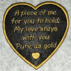 May include: Black heart-shaped embroidered patch with gold trim and text. The text reads "A piece of me for you to hold, My love stays with you Pure as gold." A small gold heart is at the bottom.