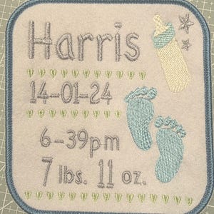 May include: Embroidered baby announcement with the name "Harris", birthdate, time, and weight. Features a baby bottle, footprints, and star accents. The border is blue, and the text is in gray and blue.