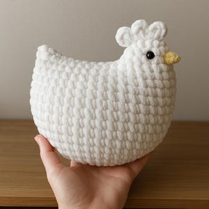 Könnte beinhalten: Weißes gehäkeltes Hühner-Plüschtier mit gelbem Schnabel und schwarzen Augen.