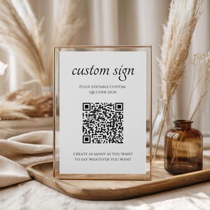 May include: A framed white sign with the text "custom sign" and a QR code. The sign also includes the phrases "FULLY EDITABLE CUSTOM QR CODE SIGN" and "CREATE AS MANY AS YOU WANT TO SAY WHATEVER YOU WANT."