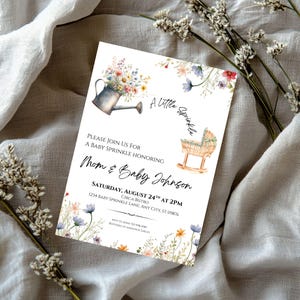 Peut inclure: Invitation pour une baby shower avec des illustrations florales et le texte "A Little Sprinkle". L'invitation comprend un arrosoir rempli de fleurs, un berceau et les d&eacute;tails de l'&eacute;v&eacute;nement. L'invitation est sur fond blanc.