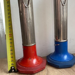 May include: Two cylindrical flashlights with metallic bodies and colored bases and caps. One is red and one is blue. A yellow measuring tape is positioned next to the red flashlight, showing a height of approximately 10.5 inches for the unit.