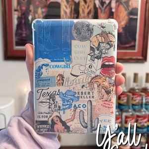 以下が含まれることがあります： カウボーイブーツ、サボテン、カウガール、そして「カウガールクラブ」と「ハウディ」の文字を含む、カラフルな画像のコラージュが施された白い携帯電話ケース。