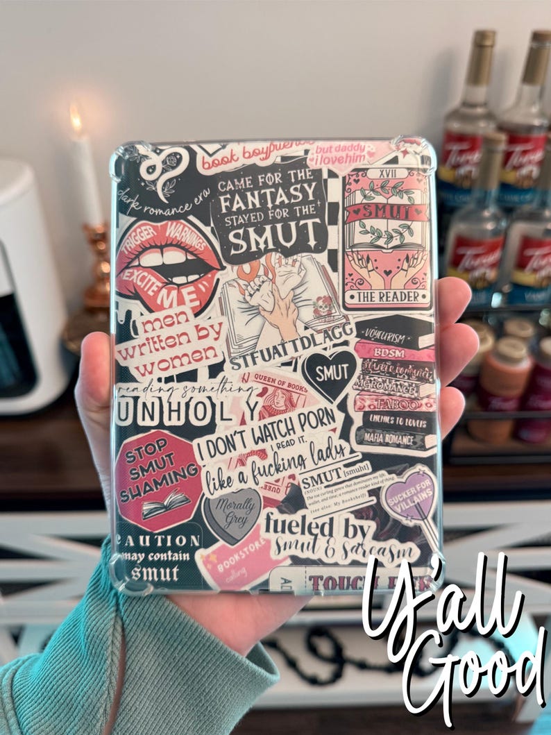 May include: A clear phone case with a variety of colorful stickers featuring phrases like "Came for the Fantasy Stayed for the Smut", "I Don't Watch Porn I Read It", "Stop Smut Shaming", and "Fueled by Smut & Sarcasm".