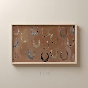 May include: Abstract painting of horseshoes in various colors, including blue, black, and white, on a brown background. The artwork is framed in a light wood frame. The text "TV art" is visible in the bottom right corner.