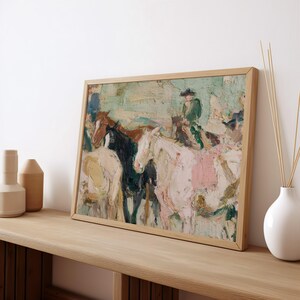 May include: An oil painting in a light wood frame depicts a group of horses and riders. The artwork features a palette of soft colors, including white, pink, brown, and green. The painting is displayed on a wooden surface.