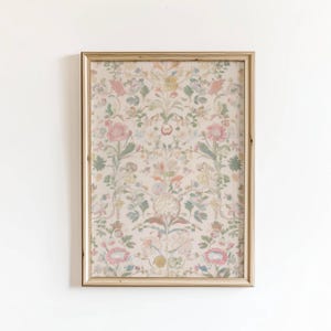 May include: A framed floral print with a gold-colored wooden frame. The print features a symmetrical pattern of flowers in shades of pink, green, yellow, and peach on a cream background. The artwork is displayed against a white wall.