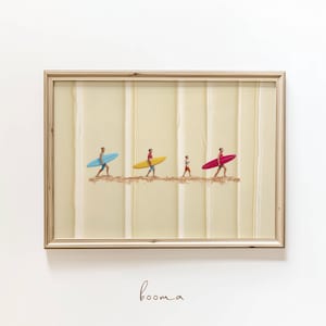 Puede incluir: Obra de arte enmarcada que representa a cuatro figuras que llevan tablas de surf. Las tablas de surf son azules, amarillas y rojas. El fondo es una superficie texturizada de color crema con líneas verticales. La obra está enmarcada en un marco de madera marrón claro. La palabra "booma" está escrita en cursiva en la parte inferior.