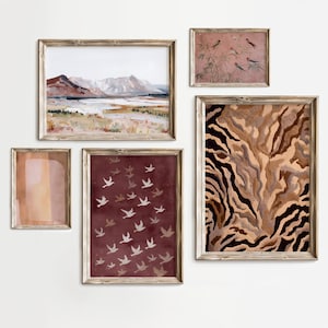May include: A gallery wall set of five framed prints featuring a landscape with mountains, a small botanical scene with birds, a solid peach-toned rectangle, a deep red print with white birds in flight, and a large abstract brown and black tiger-stripe pattern.