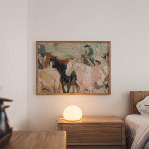 May include: A framed painting of horses and riders hangs above a wooden nightstand. The painting features a palette of pink, brown, black, and white. A round, glowing lamp sits on the nightstand, next to a bed with a wooden frame.