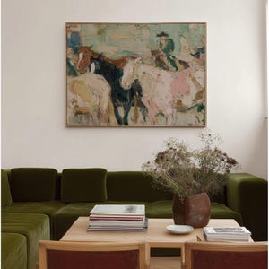 May include: An abstract oil painting in a light wood frame depicts horses and riders in a field. The artwork features a palette of muted greens, pinks, and browns. The painting hangs above a green velvet sectional sofa.