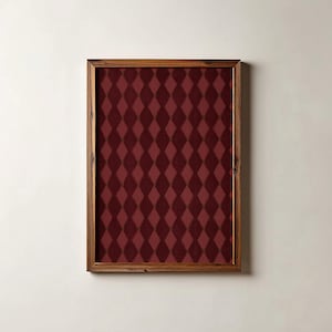May include: A framed artwork featuring a repeating diamond pattern in shades of burgundy and maroon. The artwork is encased in a natural wood frame, adding a touch of warmth to the piece. The design is symmetrical and visually engaging.
