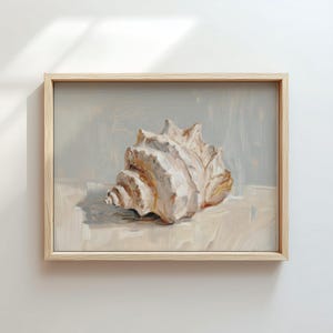 Op de afbeelding: Een ingelijst schilderij van een grote zeeschelp, weergegeven in crème, beige en bruine tinten. De achtergrond is een gedempt grijs en de lijst is van lichtkleurig hout. Het kunstwerk is een stilleven, dat de ingewikkelde details van de schelp vastlegt.
