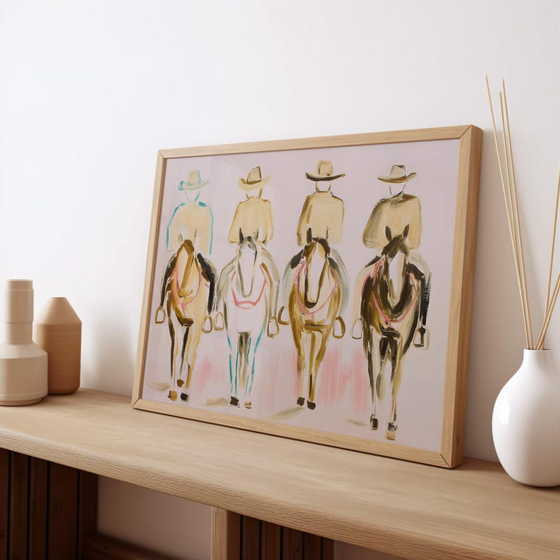 May include: A framed art print featuring an abstract painting of four riders on horseback. The riders wear hats and are depicted in neutral tones. The horses are in shades of brown, with pink and blue accents. The artwork is displayed on a wooden shelf.