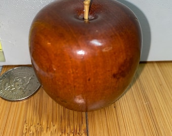 Könnte beinhalten: Ein Holzapfel mit braunem Finish und kleinem Stiel. Der Apfel liegt auf einer Holzoberfläche. Eine Silbermünze liegt neben dem Apfel.