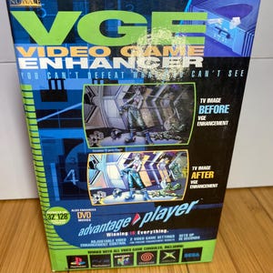 May include: A boxed VGE Video Game Enhancer. The box is primarily black, blue, and green, with the product name in large, bold, neon green letters. The box features before and after images of enhanced gameplay. The text "Winning is Everything" is also visible.