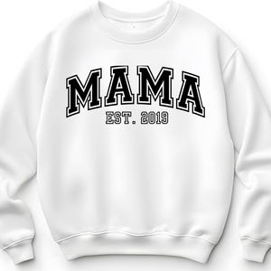 May include: White sweatshirt with the word "MAMA" in bold, black, collegiate-style lettering. Below the word "MAMA" is the text "EST. 2019" in a smaller, black font. The sweatshirt has a crew neck and long sleeves.