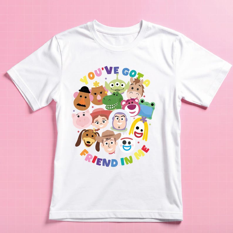 May include: A white short-sleeved t-shirt featuring a colorful graphic print of various animated characters arranged in a circular pattern. The text "YOU'VE GOT A FRIEND IN ME" is printed in multi-colored letters around the character cluster.