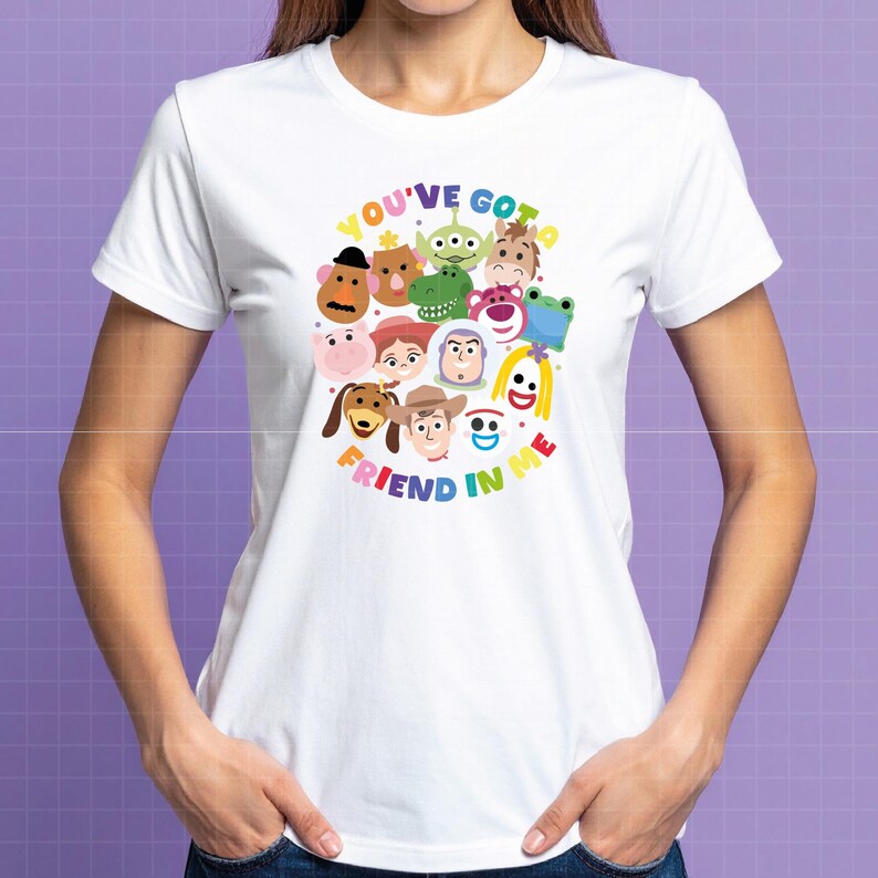 May include: A white short-sleeved t-shirt featuring a colorful graphic print of various animated toy characters arranged in a circular pattern. The text "YOU'VE GOT A FRIEND IN ME" is printed in multicolored letters around the central character cluster.