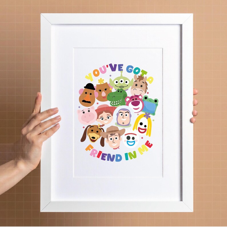 May include: A white framed print featuring a colorful illustration of various cartoon characters arranged in a circular pattern. The text "YOU'VE GOT A FRIEND IN ME" is written in multi-colored letters around the character cluster on a white background.