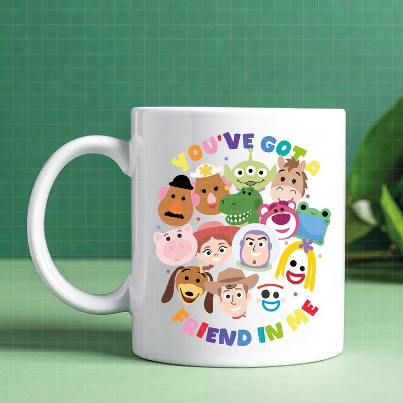 May include: A white ceramic mug featuring a colorful graphic of various Toy Story characters arranged in a circular pattern. The text "YOU'VE GOT A FRIEND IN ME" is printed in multi-colored letters arching above and below the character cluster.
