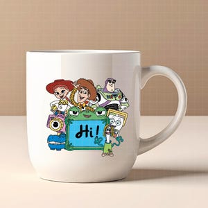 May include: White ceramic mug featuring a colorful graphic of Toy Story characters, including Woody, Buzz Lightyear, and Jessie. A green frog-like character holds a blue sign with the word "Hi!" in black. The mug has a curved handle.