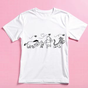 Puede incluir: Camiseta blanca con un dibujo lineal negro de los personajes de Winnie the Pooh: &Iacute;gor, Piglet, Winnie the Pooh y Tigger, con abejas y l&iacute;neas de puntos. El dise&ntilde;o est&aacute; centrado en la parte delantera de la camiseta.