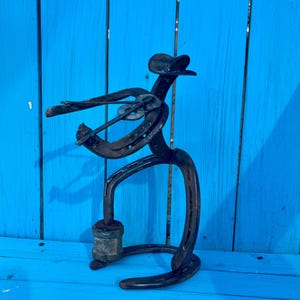 May include: A metal sculpture of a person playing a guitar made from horseshoes. The sculpture is standing on a blue wooden surface.