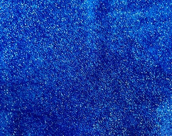 Puede incluir: Primer plano de una tela azul vibrante con una textura brillante y con purpurina. La superficie está densamente cubierta de diminutas partículas reflectantes, creando un efecto brillante. La apariencia general es un azul rico y profundo.