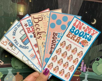 May include: A collection of colorful bookmarks with various designs and text. The bookmarks feature phrases like "Read Tea Books" and "In My Books Era," along with illustrations of books and reading-related imagery. The color palette includes blue, pink, and brown.