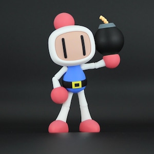 May include: A Bomberman action figure with a white head, pink antenna, and tan face. The figure wears a blue suit with a black belt and yellow buckle, white arms and legs, and pink gloves and boots. It holds a black spherical bomb with a yellow fuse.