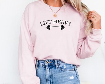 May include: A pink sweatshirt with the text "LIFT HEAVY" and a black barbell graphic.
