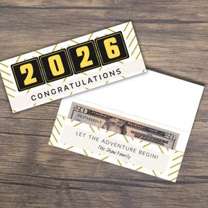 May include: A white and gold graduation card with the year 2026 in yellow and black. The card reads "Congratulations" and is next to an open white envelope with a twenty-dollar bill inside. The envelope reads "Let the adventure begin!"