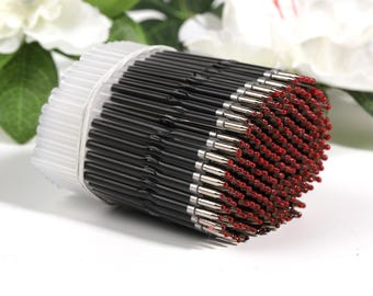 May include: A close-up of a large quantity of black and silver ballpoint pen refills with red ink tips. The refills are bundled together in a clear plastic container.
