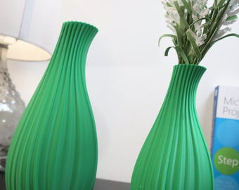 May include: Two green ceramic vases with a ribbed design. The vase on the right has white flowers.