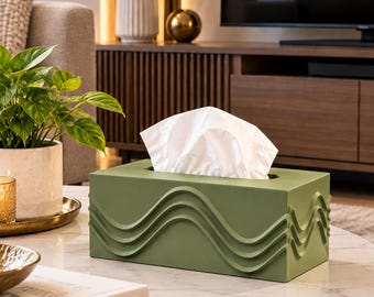 May include: A rectangular olive green tissue box cover featuring a raised, three-dimensional wave pattern along its sides. The box has a central rectangular opening at the top, from which a single white paper tissue is pulled upwards.