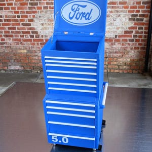May include: Blue metal toolbox with a Ford logo on the lid and "5.0" printed on the front. The toolbox has multiple drawers and is on wheels.