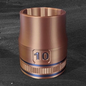 Peut inclure: Une clé à douille de couleur cuivre avec une bande bleue et le chiffre "10" en relief sur le côté. L'outil a une forme cylindrique avec un dessus et un dessous texturés.