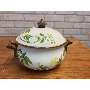 May include: White enamelware pot with lid, featuring a floral design in green and yellow. The pot has brass-colored handles and a matching knob on the lid. The pot is approximately 10 inches in diameter.