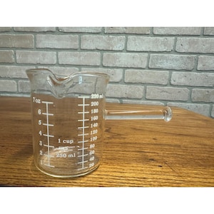 May include: A clear glass measuring cup with a handle. The cup has measurements in ounces and milliliters, with a maximum capacity of 7 oz and 220 ml. The cup is designed for accurate liquid measurement.