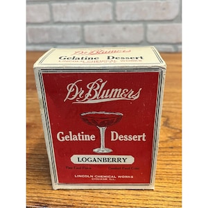 May include: A rectangular cardboard box of Dr. Blumers Gelatine Dessert in Loganberry flavor. The box is red and cream with black text, featuring a graphic of a stemmed glass. Text includes Dr. Blumers, Gelatine Dessert, Loganberry, and Lincoln Chemical Works Chicago, U.S.A.