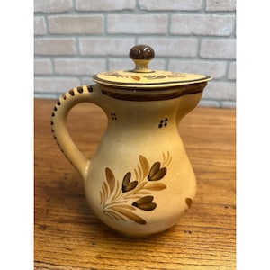 May include: A white ceramic mug with a black handle and the text "But First, Coffee" in a bold, black font. The mug is set against a blurred background, suggesting a cozy setting.