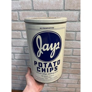 May include: Vintage Jays Potato Chips tin with a white and blue design. The tin features the Jays logo in a blue circle, with "POTATO CHIPS" below. The text "Can't stop eating em" is also visible.