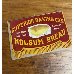 May include: Vintage sign for Holsom Bread, featuring a loaf of bread in a wrapper. The sign is red with yellow and white text, including "Superior Baking Co's" and "Made Clean, Sold Clean, Delivered Clean". The sign has a decorative yellow border.