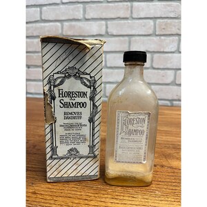 May include: A vintage Floreston Shampoo bottle and its original cardboard box. The clear glass bottle has a black cap and a paper label reading Floreston Shampoo Removes Dandruff. The box features diagonal stripes and matching text.