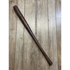 May include: A vintage wooden baseball bat with a dark brown finish. The bat has a textured surface and a rounded end. The bat is lying on a wooden surface.