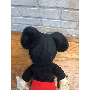 May include: Vintage Mickey Mouse soft toy. The toy features a black head with large ears, a black body, red shorts, and white gloves. The toy is made of soft, plush material and is a classic Disney collectible.