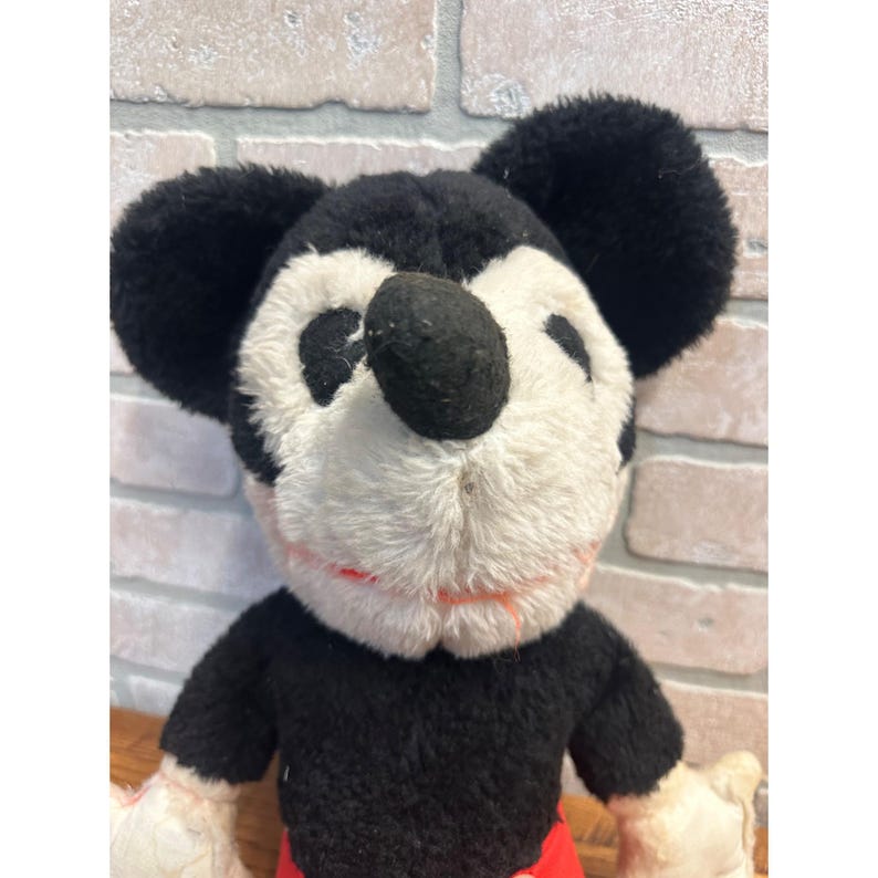May include: Vintage Mickey Mouse soft toy. The toy has a black body, ears, and nose, with a white face and red shorts. The design is classic, suggesting it's from an earlier period.