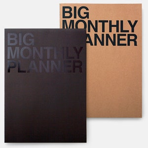Könnte beinhalten: Zwei "Big Monthly Planner" Notizbücher. Eines ist schwarz mit schwarzem Text, das andere ist hellbraun mit schwarzem Text. Die Notizbücher sind rechteckig und haben ein minimalistisches Design. Der Text ist groß und zentriert auf dem Cover.